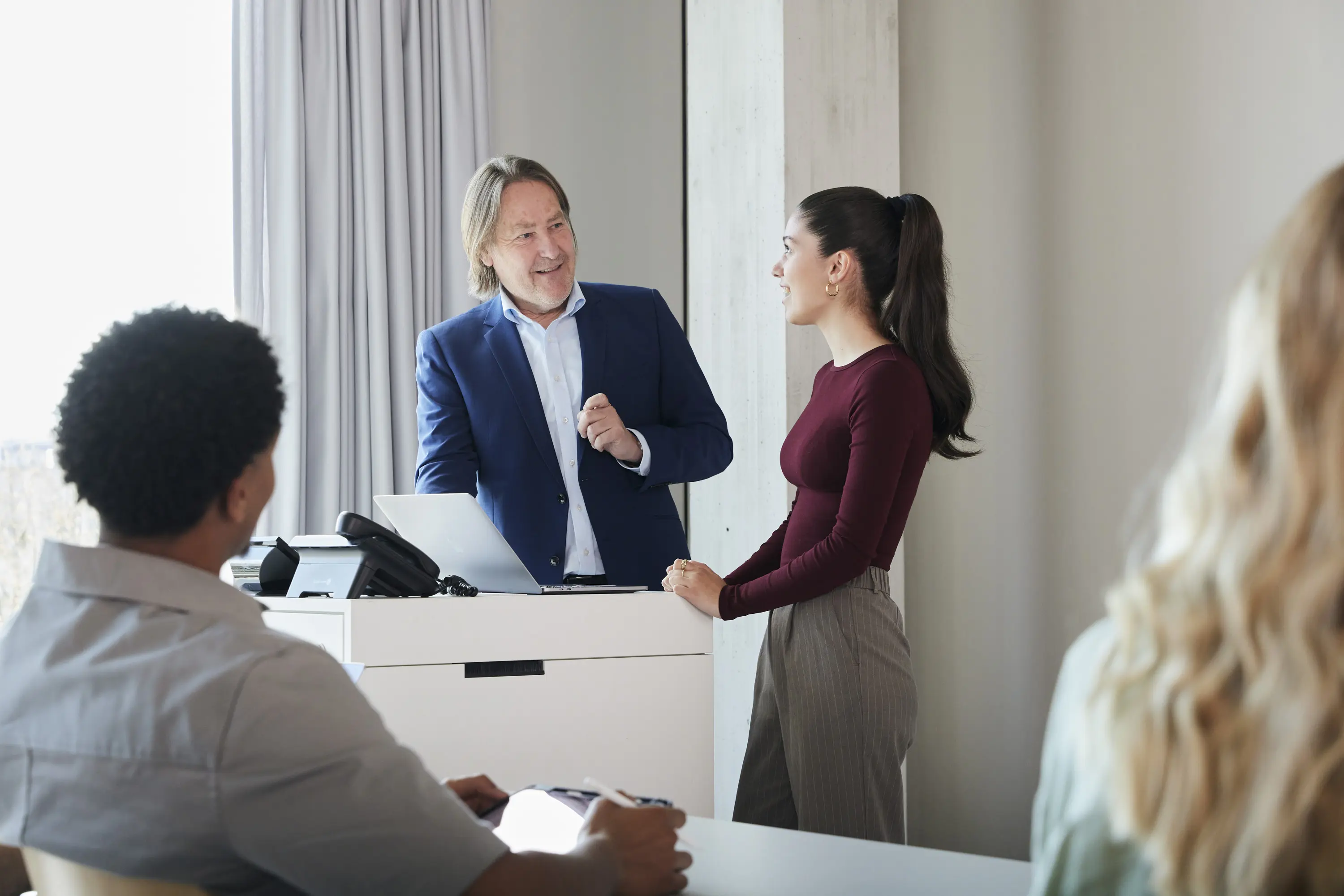Ein Professor unterhält sich in einer Vorlesung mit einer Studentin am Pult.
